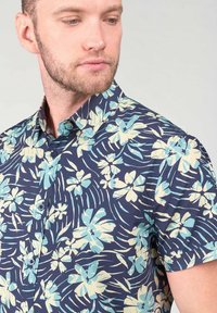 Camisa de manga corta en tela azul marina con un patrón floral en azul claro y crema, con cuello abotonado y textura suave.
