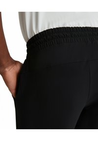 Zwarte broek met een elastische tailleband, voorzien van zijzakken en een gladde, rekbare stof. Het ontwerp is aansluitend bij de taille.
