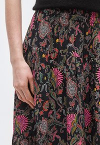 Czarna spódnica z tkaniny z żywymi wzorami kwiatowymi w kolorach różowym, czerwonym i zielonym. Projekt obejmuje warstwową konstrukcję i delikatne detale.