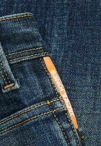 Tessuto in denim blu scuro con etichetta JACK & JONES arancione. Presenta cuciture arancioni a contrasto e un design minimalista della tasca.