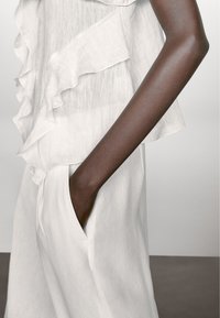 Witte, gerimpelde blouse van een lichte, gestructureerde stof, gecombineerd met losse witte broek met zijzakken.