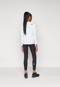 Top blanco de manga larga con logo en la parte trasera, leggings negros y zapatillas deportivas negras. Textura suave, diseño entallado y marca sutil en los leggings.