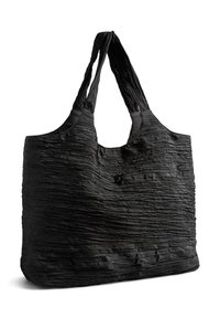 Sac cabas noir texturé avec de larges anses et un tissu froissé et souple, se tenant debout sur un fond blanc.