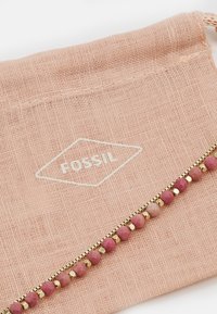 Pink fabric pouch featuring the white text "FOSSIL" in a diamond shape. Accented with a gold zipper and pink, round beads.