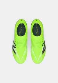 Baskets de sport vert citron avec une tige synthétique lisse, des rayures noires et une semelle texturée. Équipées de lacets plats et d'un design ajusté.