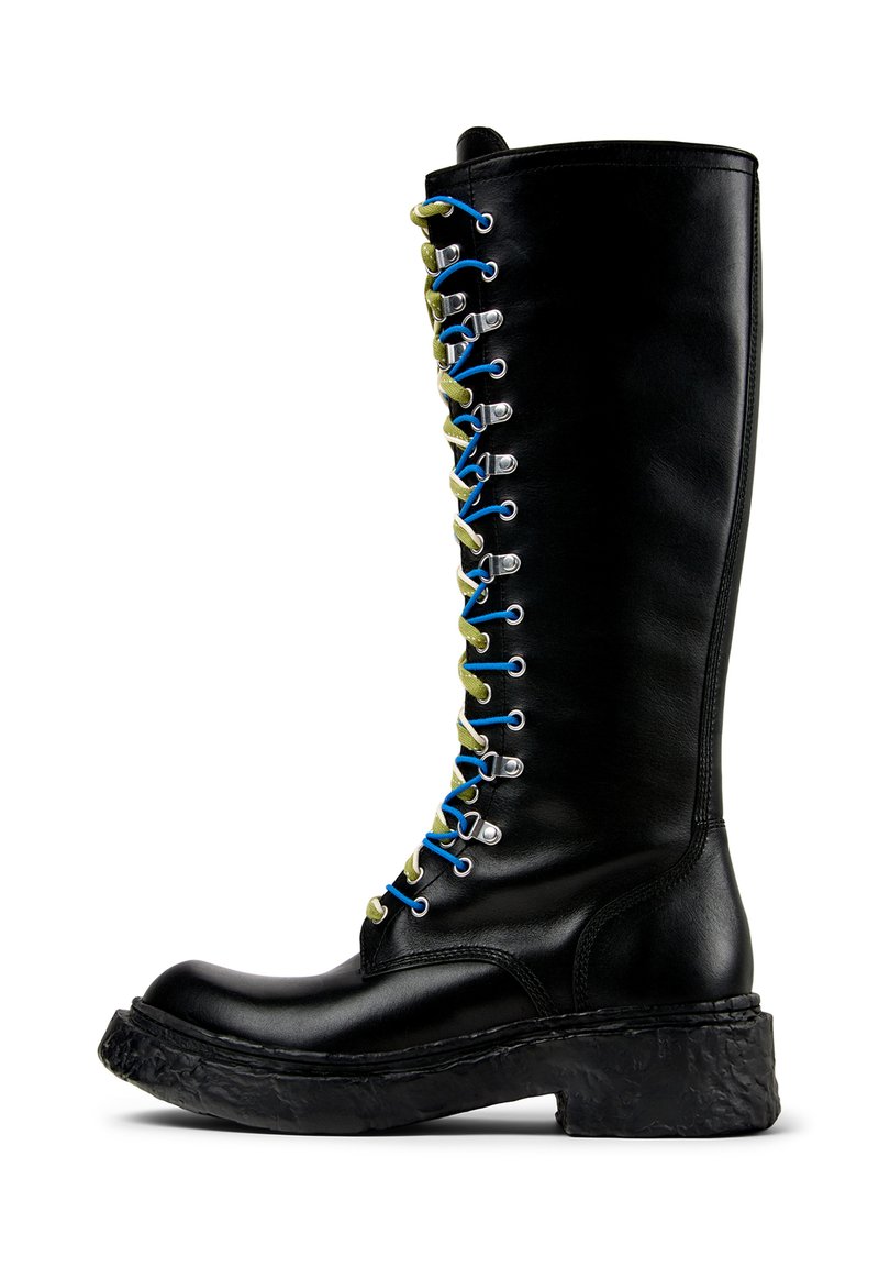 Bota de cuero negro hasta la rodilla con una suela de plataforma texturizada. Presenta cordones multicolores asegurados con ojetes plateados para ajustar.