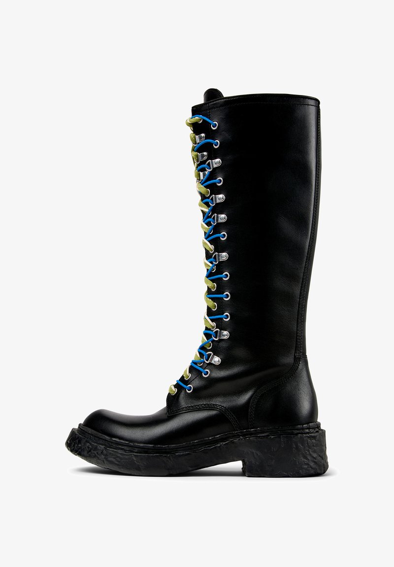 Stivale in pelle nera alto fino al ginocchio con una suola piatta testurizzata. Presenta lacci multicolori fissati con occhielli argentati per la regolazione.