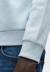 Lichtblauwe sweatshirt met geribbelde manchetten, met een gladde textuur en een ontspannen pasvorm, gecombineerd met donkerblauwe denim.