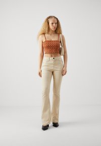 Jeans de campana beige combinados con un top corto naranja con estampado. El top presenta líneas onduladas, mientras que los jeans están hechos de denim suave.