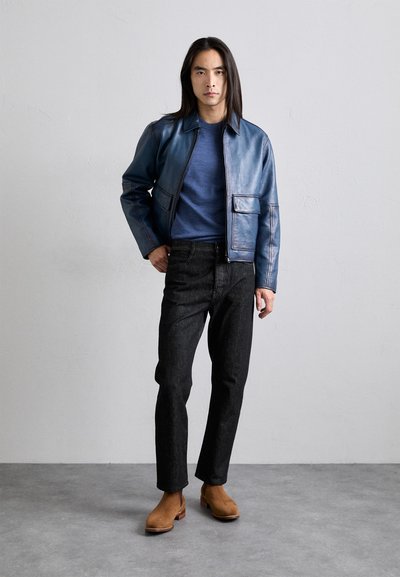 Chaqueta de cuero azul con cuello alto, cierre de cremallera y bolsillos laterales; combinada con jeans de mezclilla grises y botas de tobillo marrones. Fondo plano.