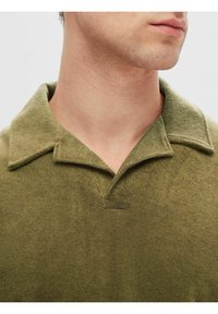 Polo shirt vert olive en tissu texturé, avec un col classique et une patte de boutonnage partielle pour un ajustement décontracté.