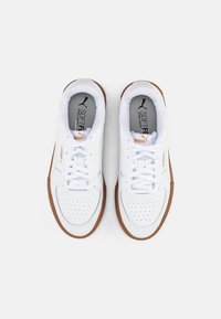 Zapatillas Puma blancas con suelas marrones, atadas, vistas desde arriba sobre un fondo claro y liso.