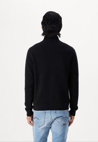 Black knitted sweater with a high collar, ribbed cuffs, and hem. The back view shows a fitted design, paired with light blue denim jeans.