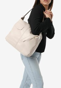 Borsa a tracolla in pelle beige chiaro con una texture liscia, dotata di una tasca con zip e una singola tracolla. Design minimalista con un logo discreto.