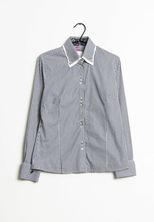 Zwart-wit geruit shirt met lange mouwen, witte kraag en manchetten, hangend aan een zwarte hanger tegen een witte achtergrond.