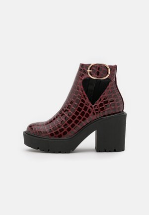 Bottine bordeaux embossée effet croco avec talon plateforme noir épais et bride avec boucle dorée sur un panneau latéral extensible.