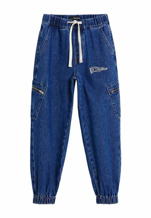 Blue denim jogger pants with elastic waist and cuffs, white drawstring, side zip pockets, and a "Desigual" logo patch on the right thigh.