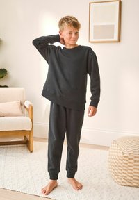 Dark gray cotton sweatshirt with long sleeves and relaxed fit, paired with matching sweatpants featuring elastic cuffs, worn barefoot.