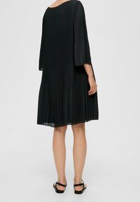 Svart plisserad klänning med trekvartsärmar, lös passform och rundad halsringning. Slät textur med en svängande silhuett.