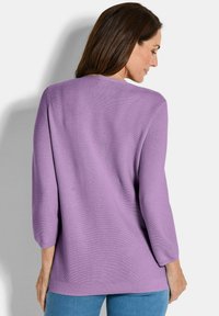 Lavendelfarbener, lockerer Strickpullover mit Rundhalsausschnitt, dreiviertellangen Ärmeln und geripptem Saum, kombiniert mit hellblauen Jeans.