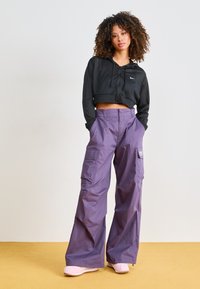 Black cropped hoodie with a mesh texture and front drawstrings, paired with loose-fitting, light purple cargo pants featuring side pockets.