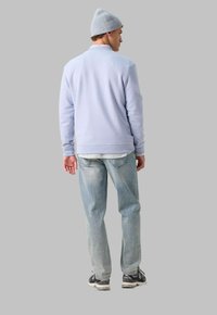 Pull en maille bleu clair, coupe décontractée, associé à un jean en denim léger. Un bonnet gris et des baskets noires complètent la tenue. Vue arrière à plat.