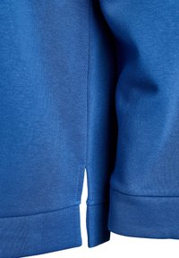 Nahaufnahme des Saums eines blauen Sweatshirts mit seitlichem Schlitz und langem Ärmelbündchen, die Stoffstruktur und Nähdetails zeigend.