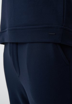 Navyblauw loungewear set bestaande uit een zachte, gestructureerde stoffen top en bijpassende broek, met een subtiele logo patch op de zoom.