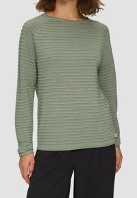 Grön ribbad långärmad topp med rund halsringning, med strukturerade horisontella ränder och en liten logotypetikett i sidsömmen.