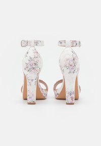 Sandali con tacco alto bianchi con motivo floreale in rosa e viola. Presentano una cintura alla caviglia e un design open-toe con superficie testurizzata.
