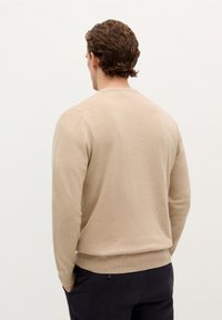 Beige Langarmpullover mit Rundhalsausschnitt, gerippten Bündchen und Saum. Weiche Textur, schlichtes Design, getragen mit dunklen Hosen.