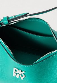 Tumesinise nahast käekott hõbedaste detailidega, millel on tõmblukuga sulgemine ja reljeefne logo. Siseosa on sile ega sisalda nähtavaid taskuid.