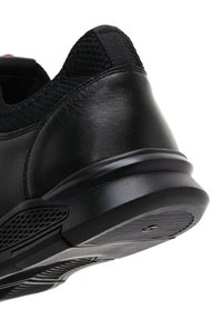 Zapatilla negra de cuero con parte superior de malla texturizada, suela de goma y diseño deportivo. Cuenta con un collar acolchado y un patrón de pisada único.
