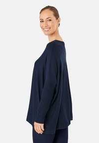 Pull en maille oversized bleu marine, avec texture côtelée, encolure large et manches décontractées. Associé à un pantalon bleu foncé.