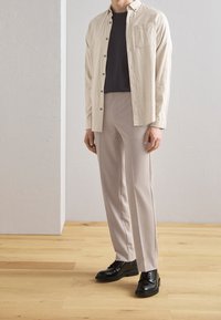 Světle béžová košile na knoflíky, tmavé tričko pod ní, světle šedé kalhoty, černé boty. Ostré textury, na míru šitý střih, minimalistický design.