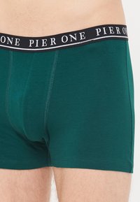 Grüne Baumwollboxershorts mit einem schwarzen Bündchen, das "PIER ONE" in weißem Text zeigt. Glatte Textur und enganliegendes Design mit kontrastierenden Nähten.