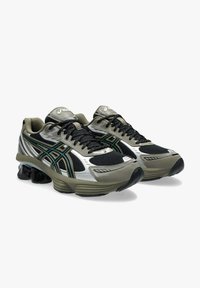 Scarpe da ginnastica nere e verde oliva con tomaia in rete, dettagli argentati, unità di ammortizzazione visibile e suola in gomma resistente.