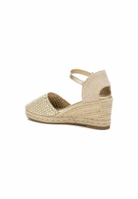 Sandalia de cuña con parte superior de oro trenzada, parte trasera a cuadros beige y correa en el tobillo. Detalles de cuerda de yute a lo largo de la suela. Diseño de punta cerrada.