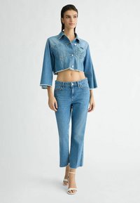 Kratka jeansa jakna s ošiljenim ovratnikom, sprednjimi žepi in razfrčenim robom; v kombinaciji s svetlo modrimi, razširjenimi jeans hlačami z nepravilnim robom.