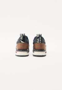 Vue arrière de baskets avec un dessus bleu, des accents en cuir marron, une semelle intermédiaire blanche mouchetée et un branding bien visible sur les languettes du talon.