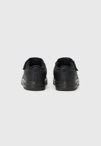 Černé tenisky Nike s koženým svrškem, polstrovaným límcem a suchým zipem. Obsahují texturovanou podrážku a logo na zadní straně.