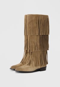 Bottes en suède à franges de couleur marron clair, avec des détails de franges superposées, un bout pointu, un petit talon empilé et une texture lisse.