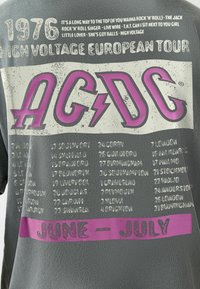 T-shirt AC/DC High Voltage Tour Européen 1976 avec le logo du groupe, les villes de la tournée, les dates en juin et juillet, et les titres des chansons listés en haut.