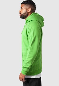Hoodie verde brillante con tasca a marsupio, cappuccio con cordini, polsini e orlo a coste. Realizzato in morbido materiale misto cotone.