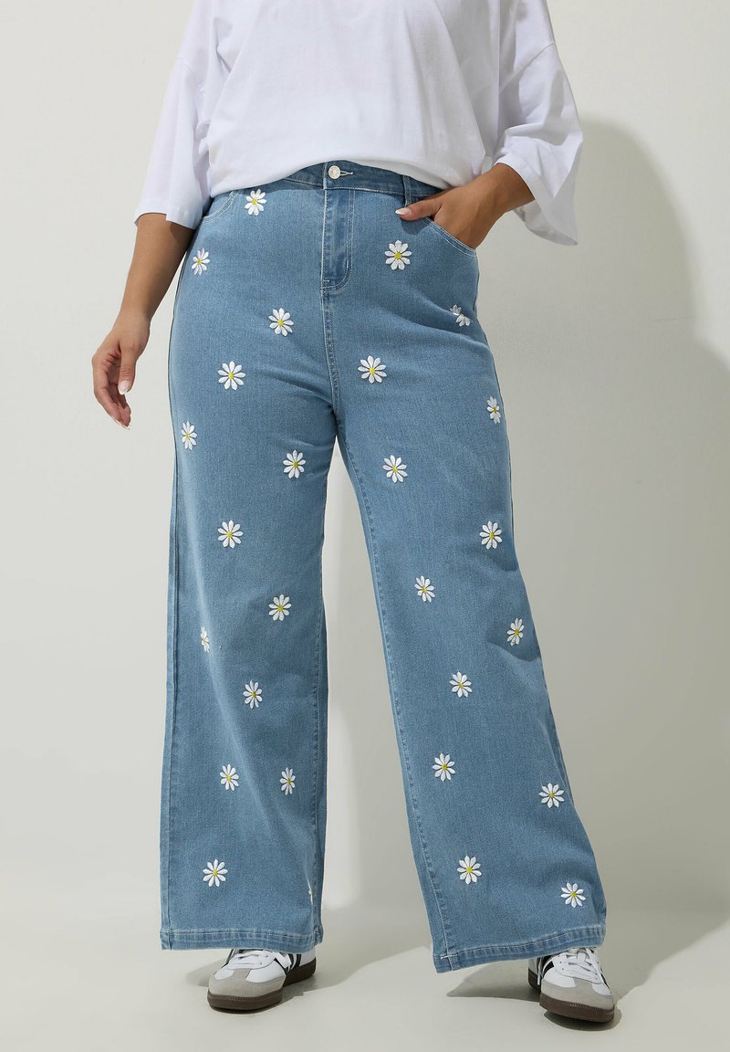 Vaaleansiniset leveälahkeiset farkut, joissa on valkoisia päivänkakkara-ompeluja ympäriinsä. Sisältää taskut ja etu-nappi sulkemisen.