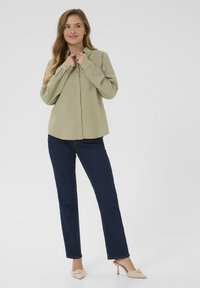Lichtgroen overhem shirt met kraag, lange mouwen en een losse pasvorm, gecombineerd met donkerblauwe rechte jeans en beige hakken.