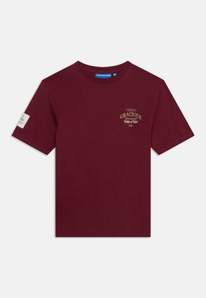 Bordeaux kortærmet T-shirt med rund hals, lille beige tekst "Gracious" på venstre bryst og et hvidt mærke på venstre ærme.