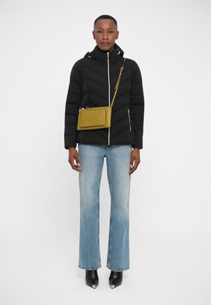 Black puffer jacket with chevron pattern, gold zippers, light blue flared jeans, and black ankle boots with metallic accents, paired with a green crossbody bag.
