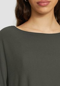 Dunkelgrüner, gerippter Pullover mit breitem Bootsausschnitt und weicher Textur, der eine lockere Passform um die Schultern betont.