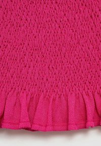 Tessuto di maglina fucsia con un motivo testurizzato e orlo arricciato. Il materiale è morbido e elastico, caratterizzato da una serie di elementi in rilievo.